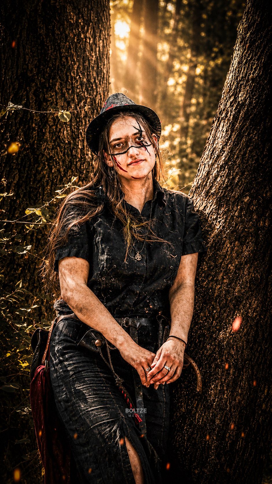 Kendra lehnt sich mit der Schulter an einen Baum und schaut verträumt in die Kamera.